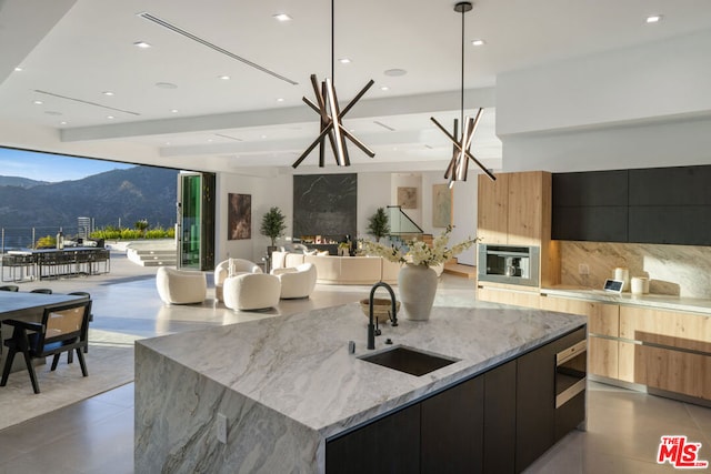 kitchen with a large island with sink, sink, stainless steel oven, a notable chandelier, and a mountain view