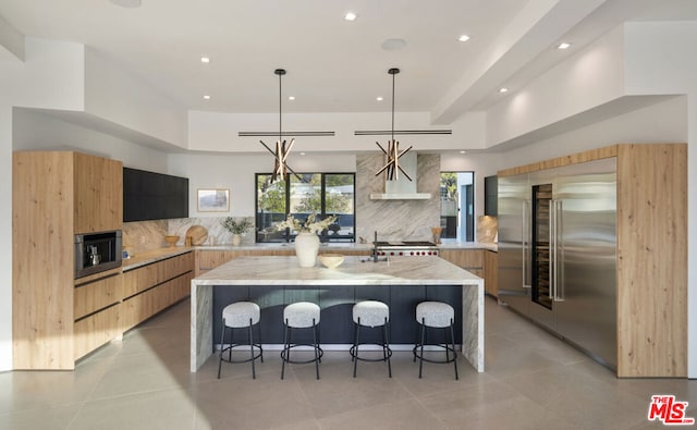 kitchen featuring light stone countertops, decorative light fixtures, built in appliances, tasteful backsplash, and an island with sink