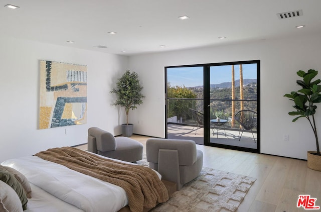 bedroom with light wood-type flooring, a mountain view, and access to outside