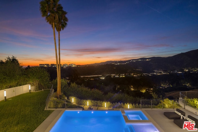 pool at dusk with a lawn and an in ground hot tub