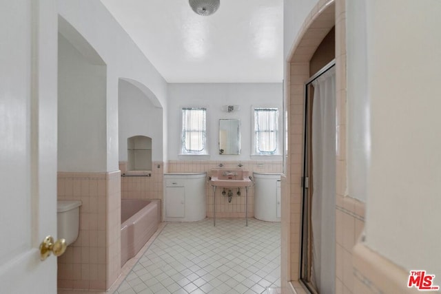 bathroom featuring a bathing tub, tile patterned flooring, tile walls, and sink