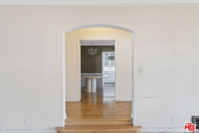 corridor featuring hardwood / wood-style floors, crown molding, and an inviting chandelier