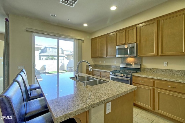 kitchen featuring sink, light stone countertops, an island with sink, a breakfast bar area, and stainless steel appliances