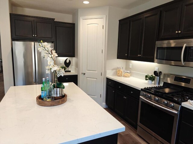 kitchen featuring stainless steel appliances, dark hardwood / wood-style floors, a center island, and light stone countertops