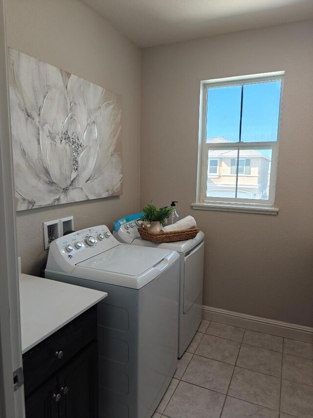 clothes washing area featuring cabinets, light tile patterned floors, and washer and clothes dryer