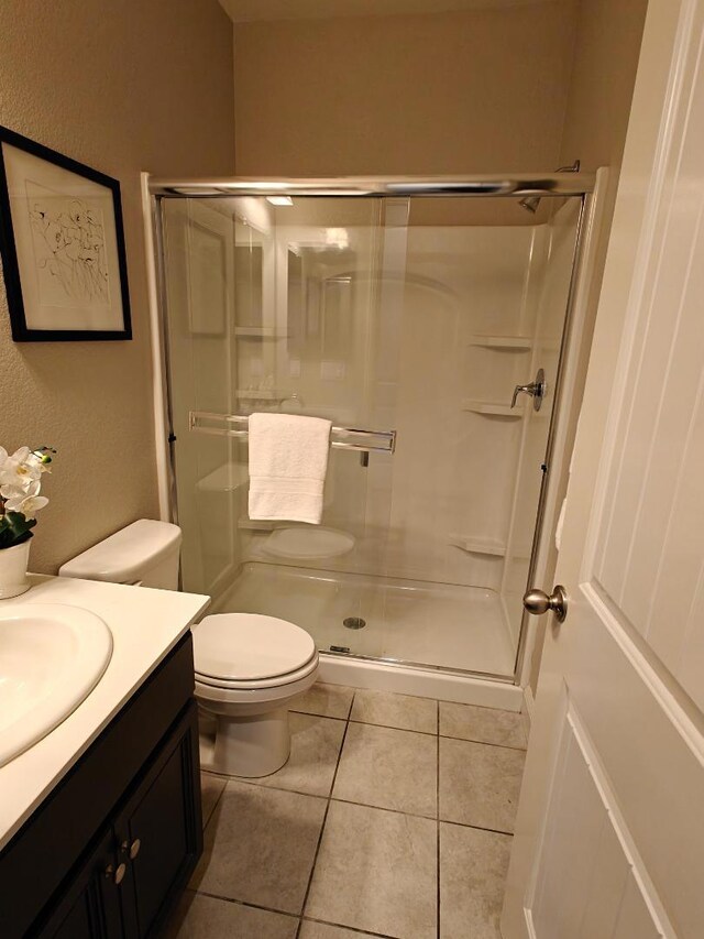 bathroom featuring walk in shower, vanity, toilet, and tile patterned flooring