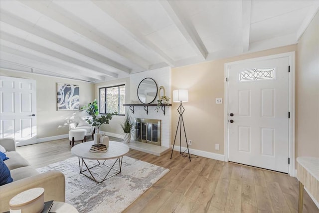 living room with a brick fireplace, light wood-type flooring, and beamed ceiling