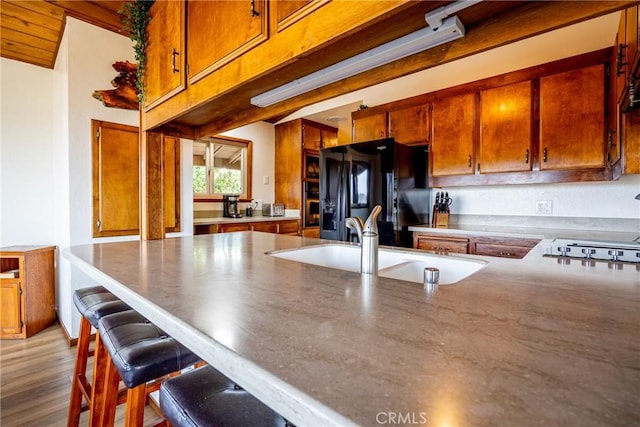 kitchen featuring black refrigerator with ice dispenser, a breakfast bar area, brown cabinets, stovetop, and a sink
