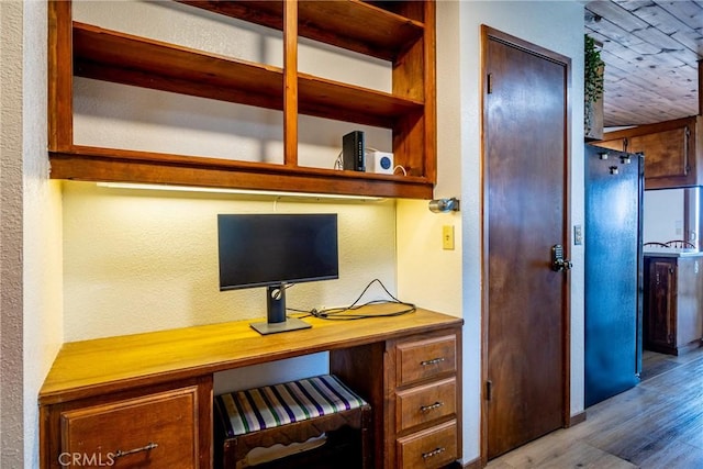 home office featuring a textured wall, built in desk, and wood finished floors
