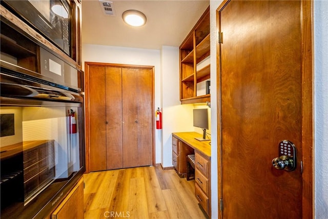 doorway to outside featuring built in study area, light wood finished floors, and visible vents