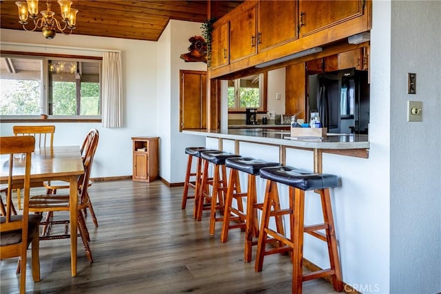 kitchen featuring a breakfast bar area, dark wood-style flooring, brown cabinets, a notable chandelier, and black refrigerator