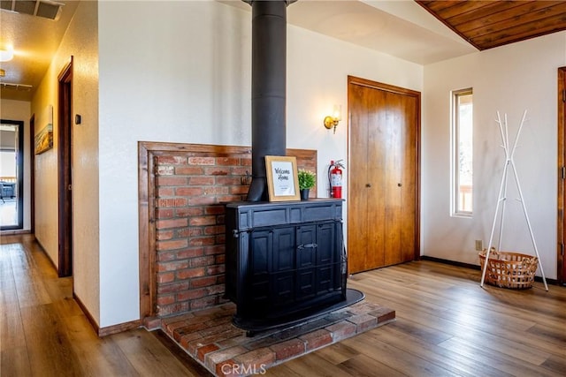interior space featuring visible vents, a wood stove, wood-type flooring, baseboards, and vaulted ceiling