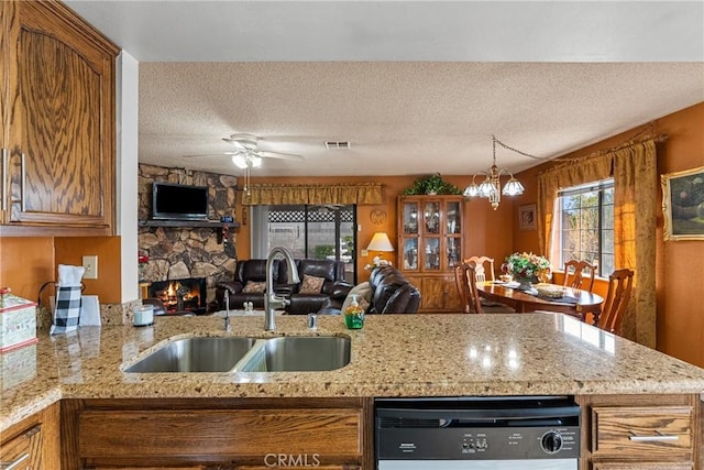 kitchen with sink, a stone fireplace, a textured ceiling, dishwashing machine, and light stone counters