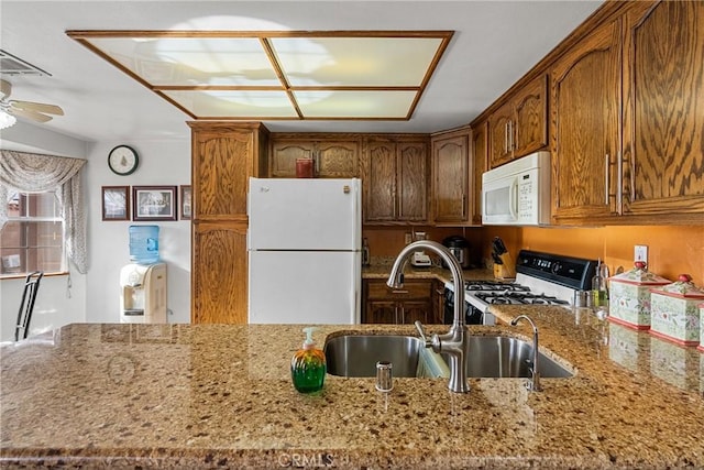 kitchen with light stone countertops, ceiling fan, sink, and white appliances