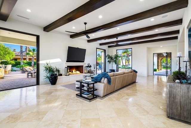 living room featuring beamed ceiling, ceiling fan, and a tile fireplace