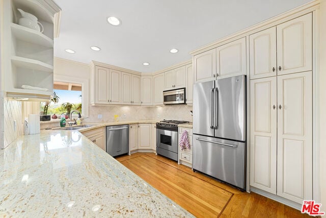 kitchen featuring appliances with stainless steel finishes, light stone counters, cream cabinets, and sink