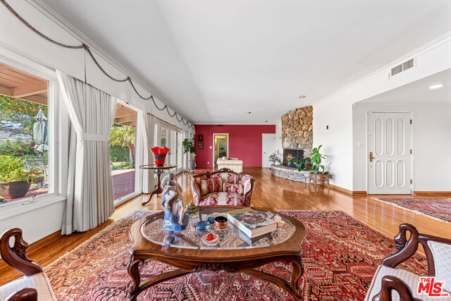 living room with light hardwood / wood-style floors, plenty of natural light, crown molding, and a stone fireplace