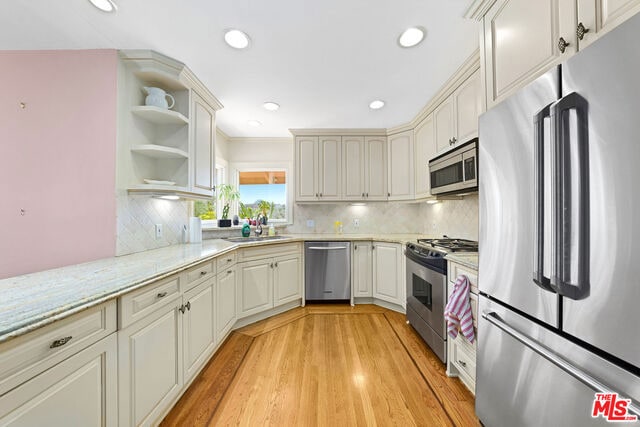 kitchen with tasteful backsplash, sink, stainless steel appliances, and light hardwood / wood-style flooring