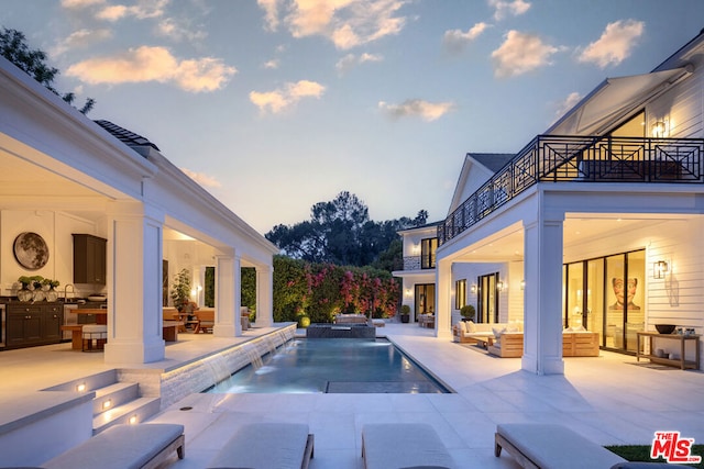 pool at dusk featuring pool water feature, outdoor lounge area, a patio, and an in ground hot tub