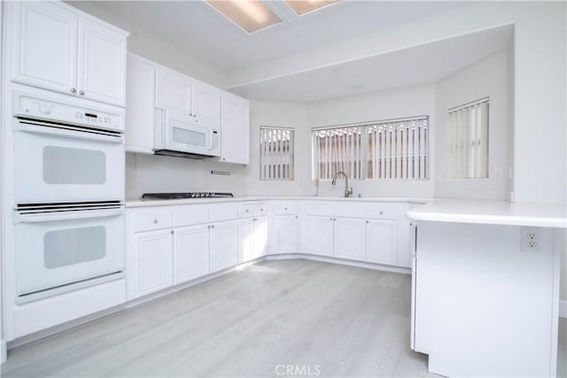 kitchen with light wood-type flooring, sink, white cabinets, and white appliances