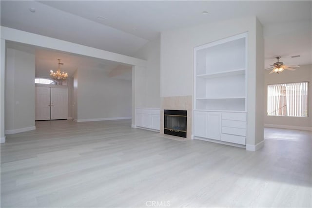 unfurnished living room with light hardwood / wood-style floors, a fireplace, vaulted ceiling, ceiling fan with notable chandelier, and built in shelves