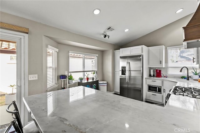 kitchen featuring light stone countertops, appliances with stainless steel finishes, lofted ceiling, white cabinetry, and a healthy amount of sunlight