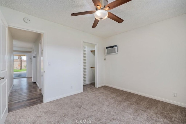 unfurnished bedroom featuring ceiling fan, an AC wall unit, a textured ceiling, a closet, and dark carpet