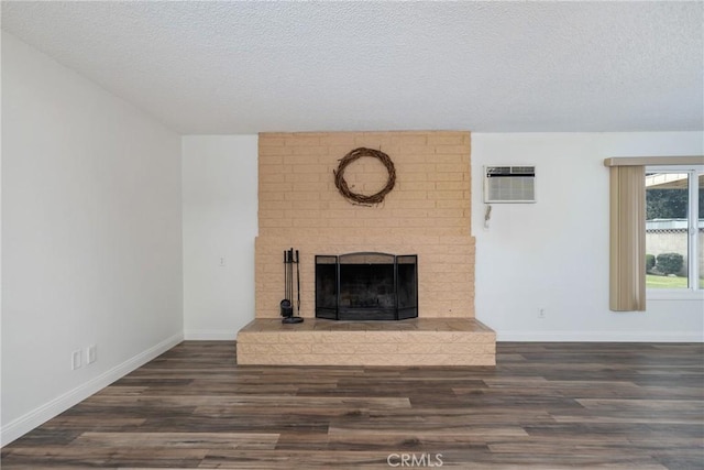 unfurnished living room with a textured ceiling, a brick fireplace, dark hardwood / wood-style flooring, and a wall mounted air conditioner