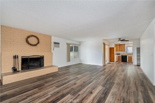 unfurnished living room featuring a brick fireplace, ceiling fan, dark hardwood / wood-style floors, a wall mounted air conditioner, and a textured ceiling