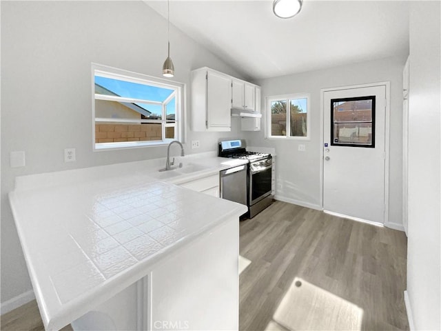 kitchen with stainless steel gas range, sink, white cabinetry, kitchen peninsula, and pendant lighting