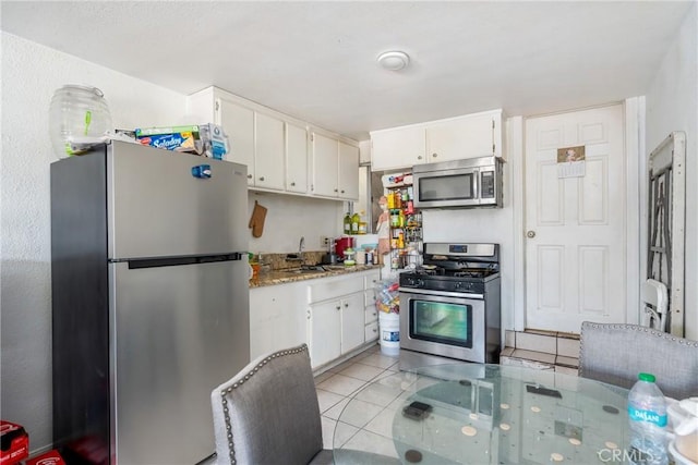 kitchen with appliances with stainless steel finishes, light tile patterned flooring, light stone countertops, white cabinets, and sink