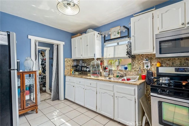 kitchen with tasteful backsplash, white cabinets, light tile patterned floors, and stainless steel appliances