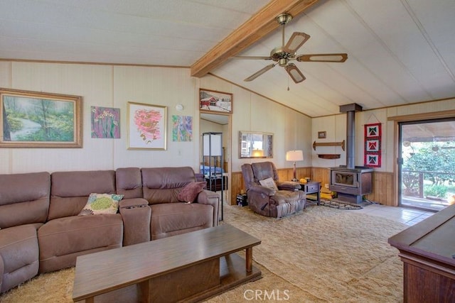 carpeted living room with ceiling fan, vaulted ceiling with beams, and a wood stove