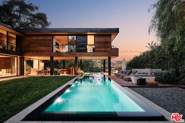 back house at dusk featuring a lawn and a balcony