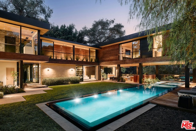 back house at dusk featuring a lawn and a pool side deck