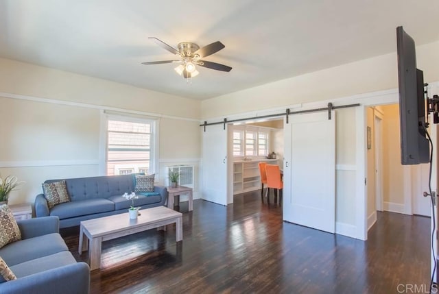 living room featuring ceiling fan, dark hardwood / wood-style floors, and a barn door