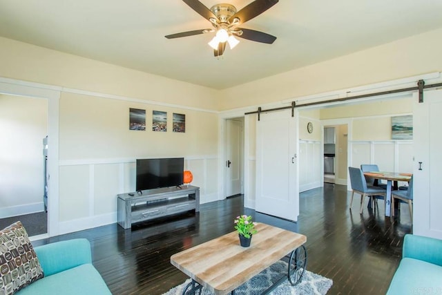 living room featuring ceiling fan, dark hardwood / wood-style floors, and a barn door