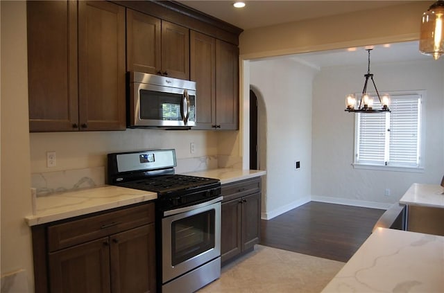 kitchen with an inviting chandelier, appliances with stainless steel finishes, decorative light fixtures, dark brown cabinets, and light stone counters