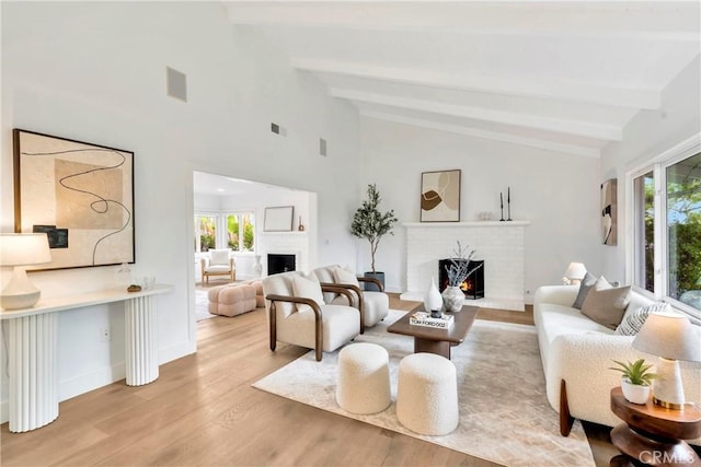 living room with lofted ceiling with beams, a brick fireplace, and light hardwood / wood-style flooring