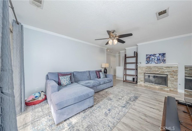 living room with hardwood / wood-style flooring, ceiling fan, ornamental molding, and a stone fireplace