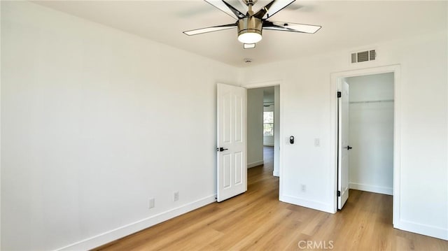 unfurnished bedroom with ceiling fan, a spacious closet, a closet, and light wood-type flooring