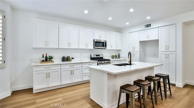 kitchen with sink, white cabinets, appliances with stainless steel finishes, and an island with sink