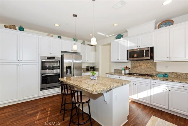 kitchen with pendant lighting, a kitchen island, white cabinetry, stainless steel appliances, and dark hardwood / wood-style floors