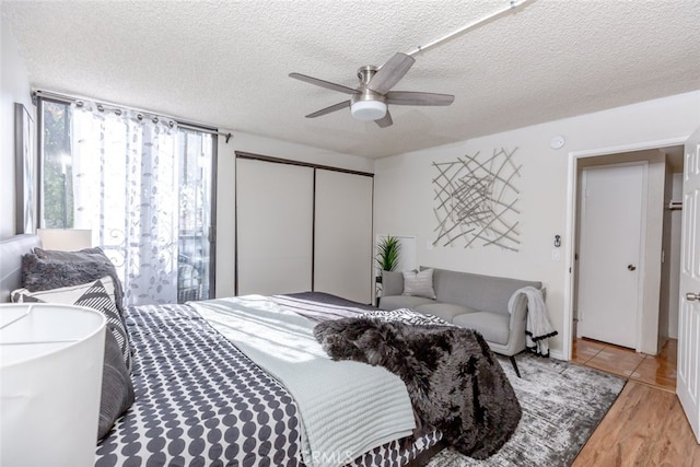 bedroom with ceiling fan, light hardwood / wood-style floors, a textured ceiling, and a closet