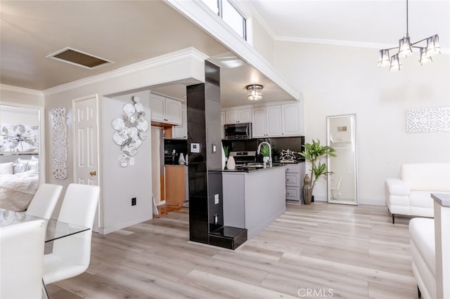 kitchen featuring decorative light fixtures, backsplash, white cabinetry, appliances with stainless steel finishes, and a chandelier