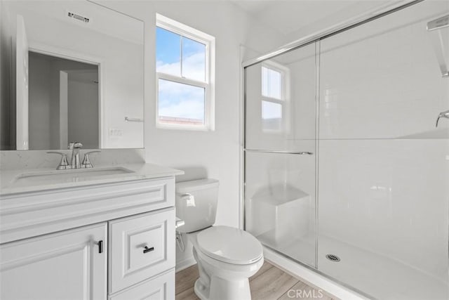 bathroom featuring toilet, wood finished floors, visible vents, vanity, and a stall shower