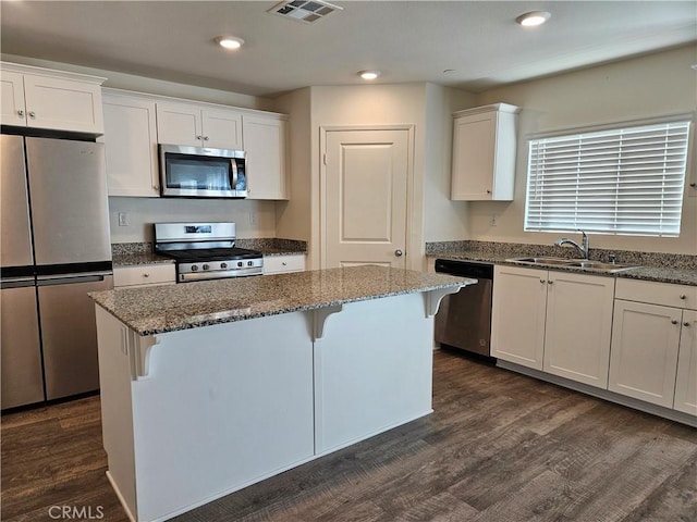 kitchen featuring visible vents, a kitchen island, appliances with stainless steel finishes, white cabinetry, and a sink