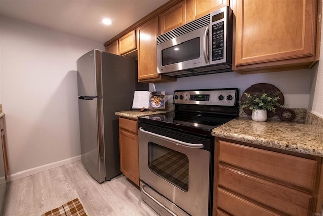 kitchen featuring light hardwood / wood-style flooring, light stone countertops, and appliances with stainless steel finishes