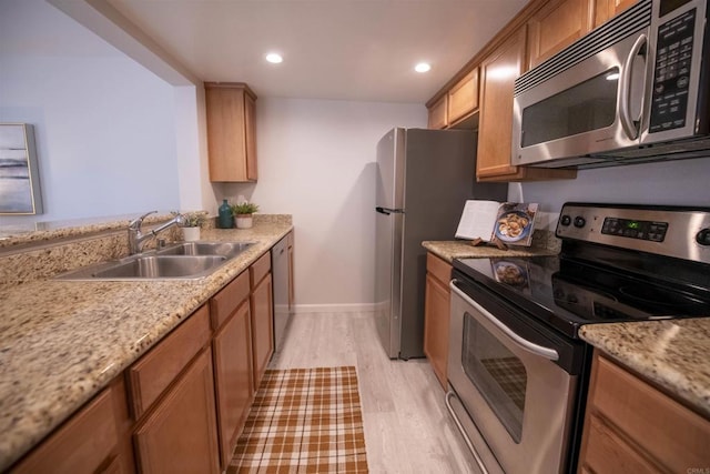 kitchen with sink, light hardwood / wood-style floors, light stone countertops, and appliances with stainless steel finishes