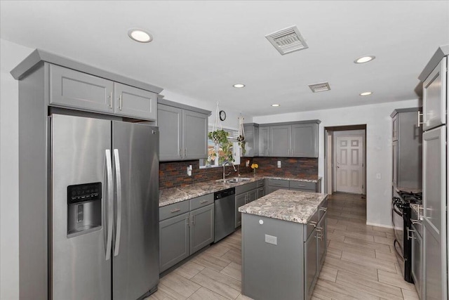 kitchen featuring a center island, sink, appliances with stainless steel finishes, gray cabinetry, and light stone counters